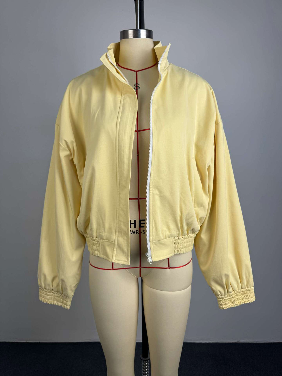 Pale yellow cropped bomber jacket, front view on mannequin, open, showing full zip and dropped shoulders