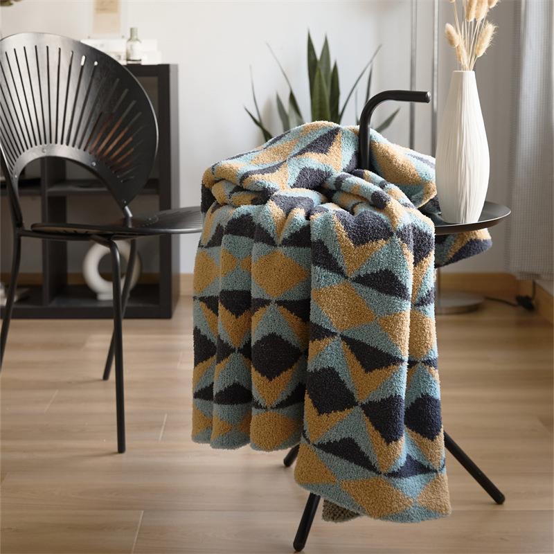 Geometric diamond-pattern knit throw in blue, mustard and charcoal, folded over chair armrest in living room setting