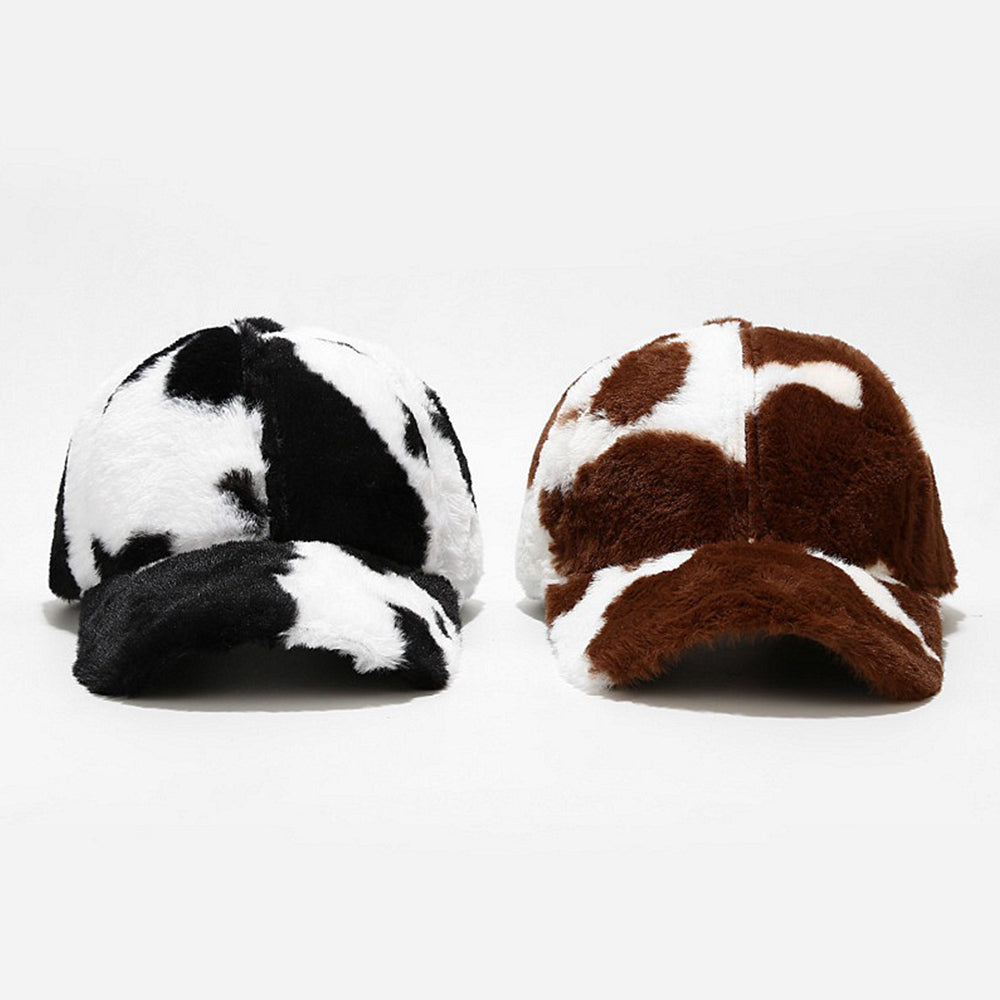 Two plush baseball caps, black-and-white cow-spot and brown-and-white cow-spot, side-by-side on white background