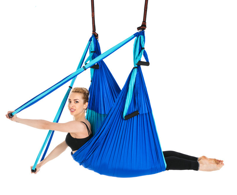 Blue aerial yoga hammock with handles, model seated in the sling holding the straps