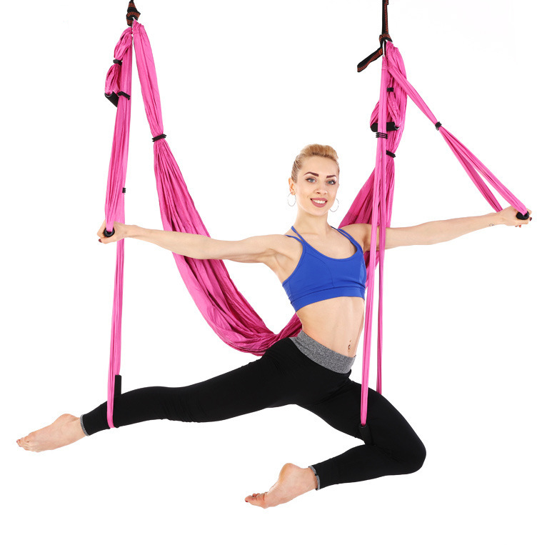 Pink aerial yoga hammock with handles, model in a wide-legged standing pose holding the straps