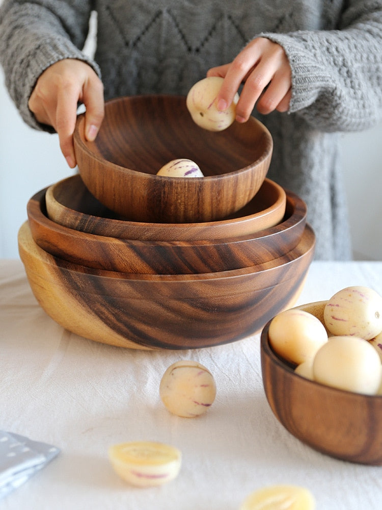 Person placing small round fruits into stacked wooden bowls with dark grain