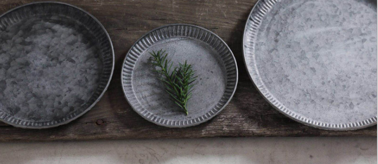 Three ribbed iron serving trays with weathered finish, in a row on wooden surface, middle one with rosemary sprig