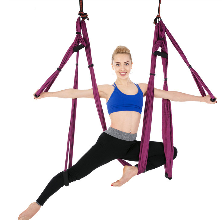 Purple aerial yoga hammock with handles, model in a split pose against a white background