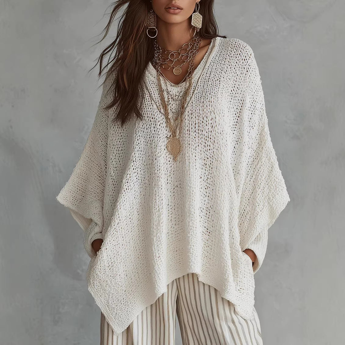 Oversized open-knit top in white, front view on model, V-neck, dolman sleeves, asymmetric hem, paired with striped pants