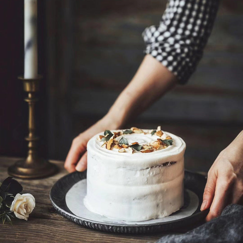Ribbed iron serving tray with weathered finish, used as cake stand, hands placing white frosted cake on it