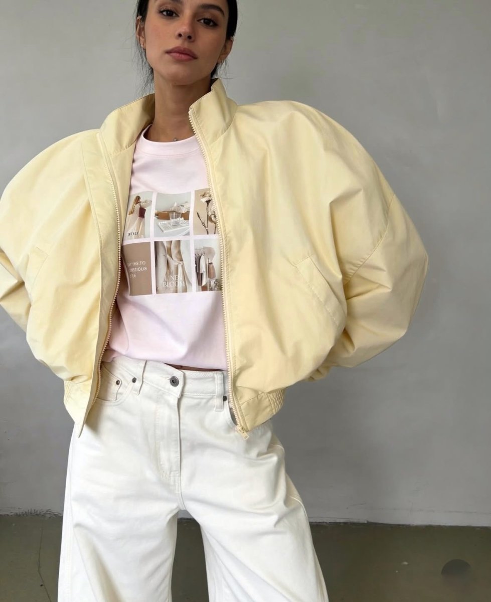 Pale yellow cropped bomber jacket, front view on model, open, dropped shoulders, over pink tee and white jeans