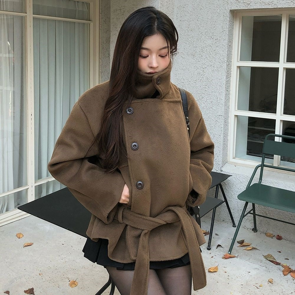 Brown cropped wrap jacket on model, front view, collar folded down, one hand in pocket, other hand at waist