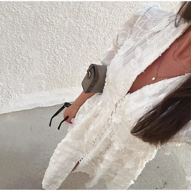 Close-up of white embroidered puff-sleeve dress with button front, showing floral pattern and V-neckline, worn by a model