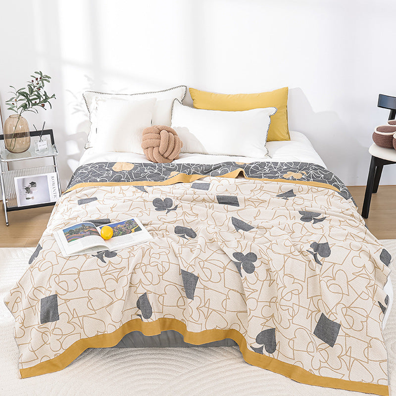 Full view of the card-suit jacquard gauze blanket laid across a bed in a bright bedroom, with pillows and a knotted cushion