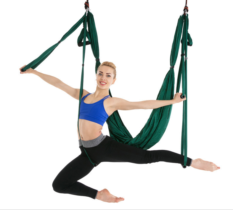 Dark green aerial yoga hammock with handles, model in a low lunge pose holding the straps