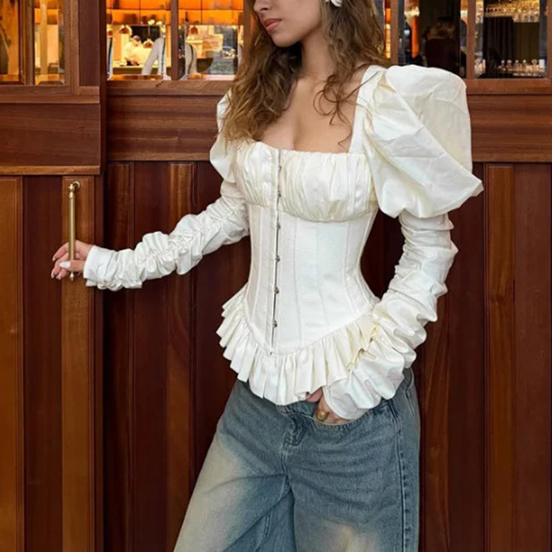 White square-neck corset top with puff sleeves and peplum hem, side view on model near wooden door