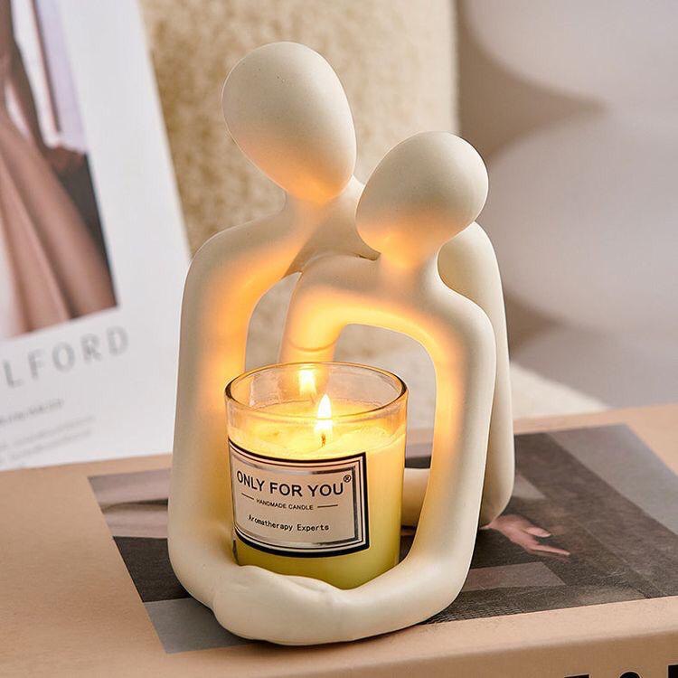 Milky white resin figurine of abstract couple, holding a lit candle in the cut-out base, on a book