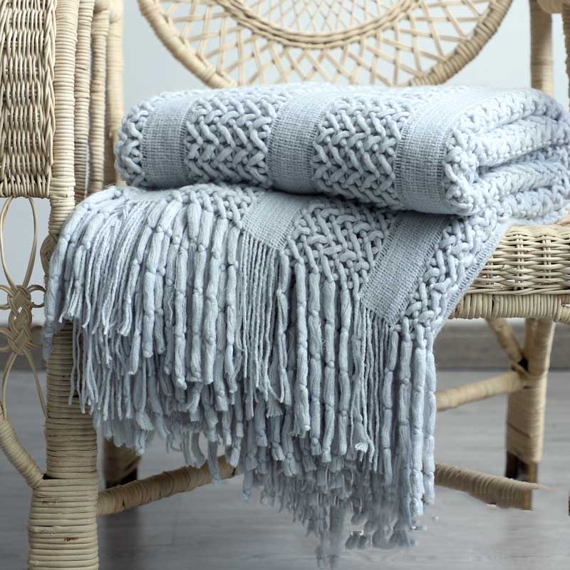 Chunky lattice knit throw in grey with tassels, folded on a wicker chair, front view