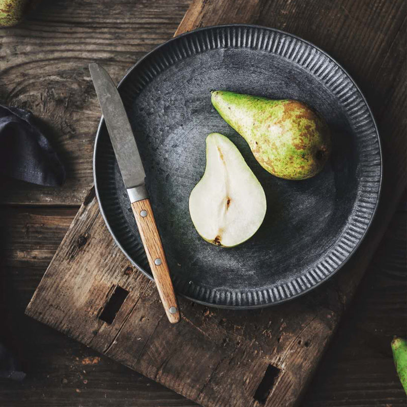 Ribbed iron serving tray with weathered finish, flat lay on wooden surface, holding a pear and knife