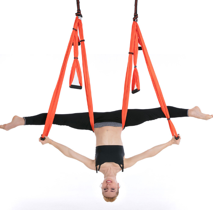 Orange aerial yoga hammock with handles, model in an inverted split pose holding the straps