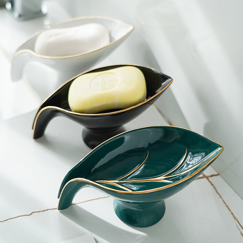 Ceramic leaf-shaped soap dish in white, black and green with gold-tone trim, arranged on a marble surface