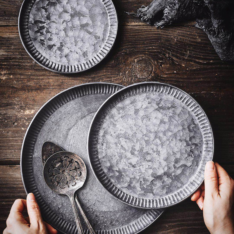Three ribbed iron serving trays with weathered finish, flat lay on wooden surface, hands holding two trays