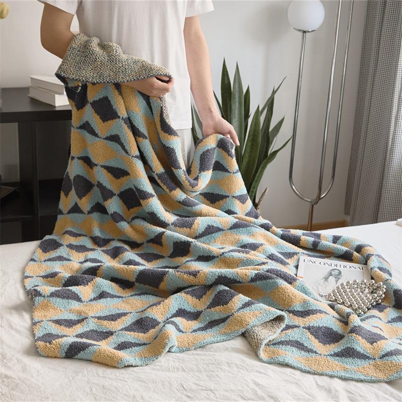 Person holding geometric diamond-pattern knit throw in blue, mustard and charcoal, showing texture and size on bed