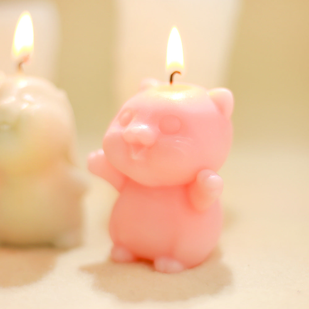 Pink cat-shaped candle lit, standing upright, with another candle blurred in background on neutral surface