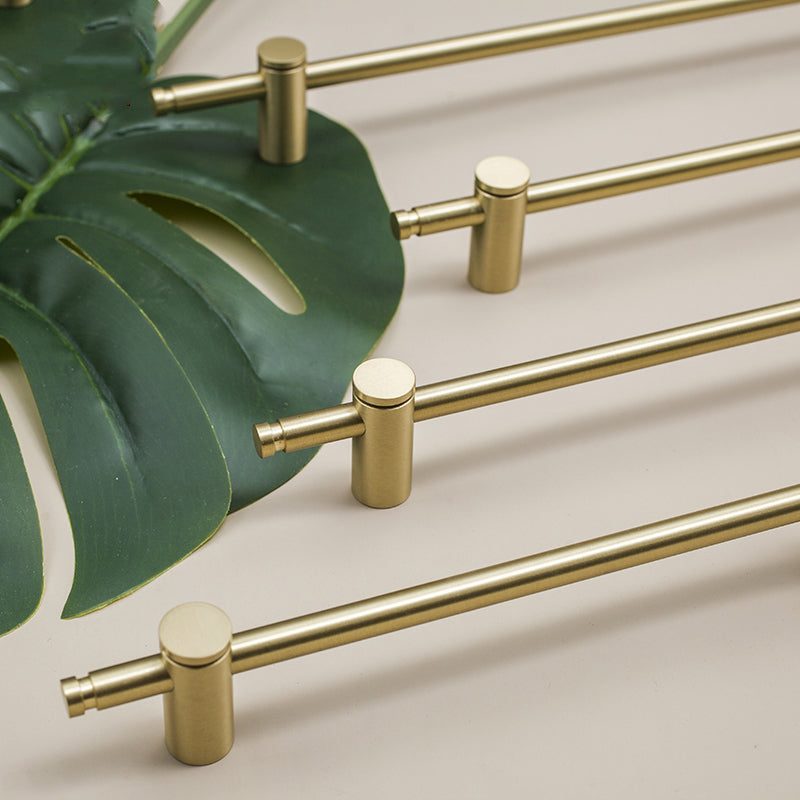 Slim bar cabinet handles in brushed gold-tone arranged diagonally with a monstera leaf, flat lay