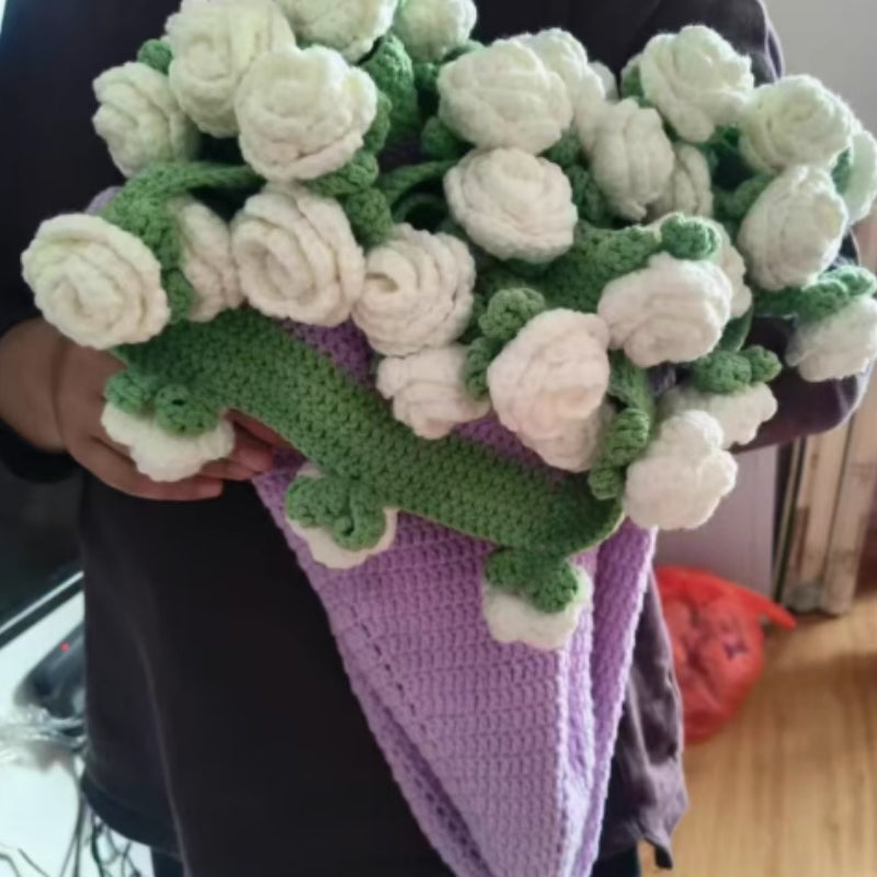 Crochet flower bouquet blanket in white flowers, folded into a bouquet shape, held by a person wearing a purple wrap, indoors