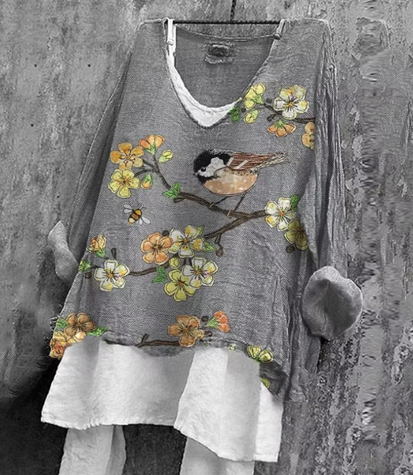Grey floral and bird embroidered V-neck tunic top with long sleeves and layered hem, front view on a mannequin against a