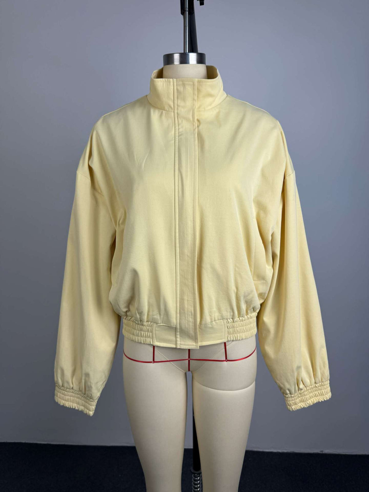Pale yellow cropped bomber jacket, front view on mannequin, zipped closed, elasticated cuffs and hem