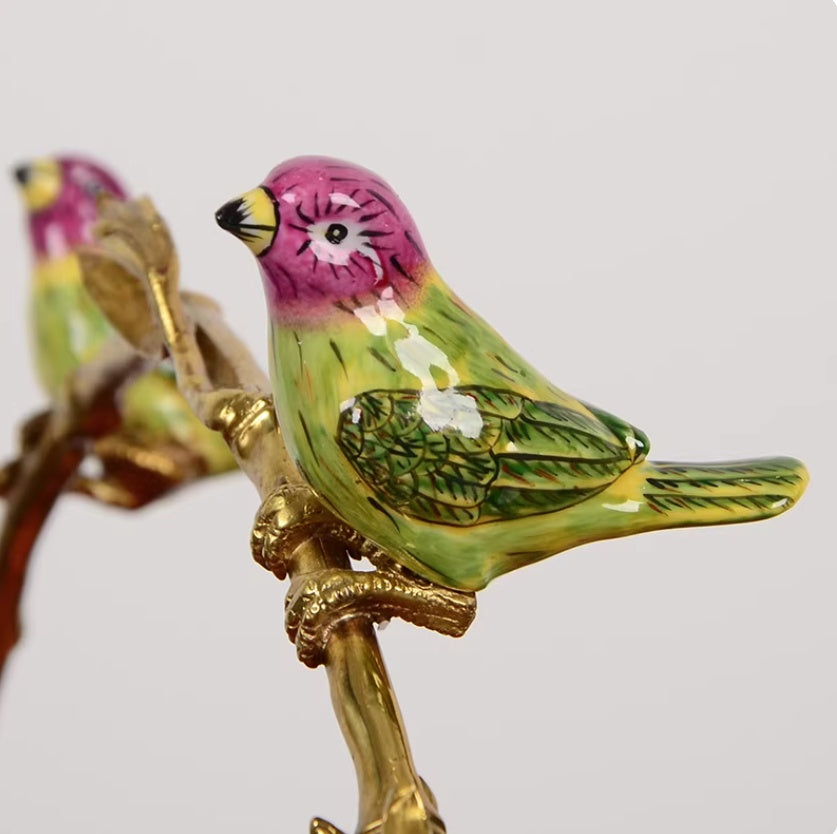 Close-up of ceramic bird with pink head, green body, perched on gilt branch
