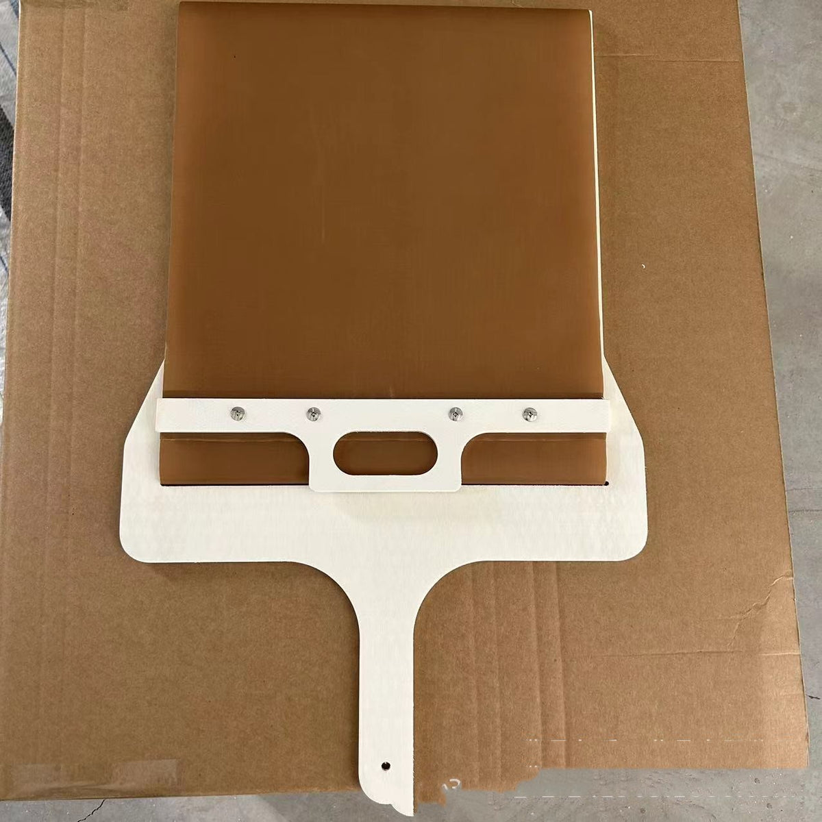 Sliding pizza peel with wooden frame, bottom view on brown cardboard surface