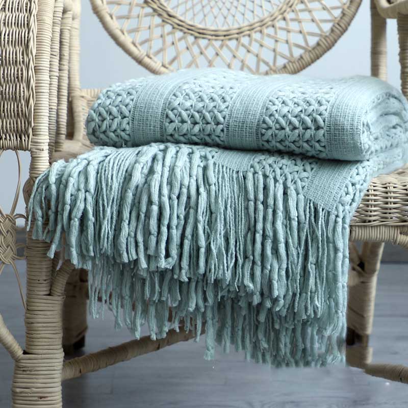 Chunky lattice knit throw in mint green with tassels, folded on a wicker chair, front view