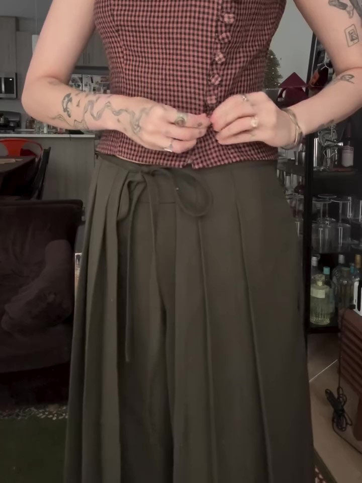 Close-up of olive wide-leg trousers with tie waist, showing front closure and fabric drape
