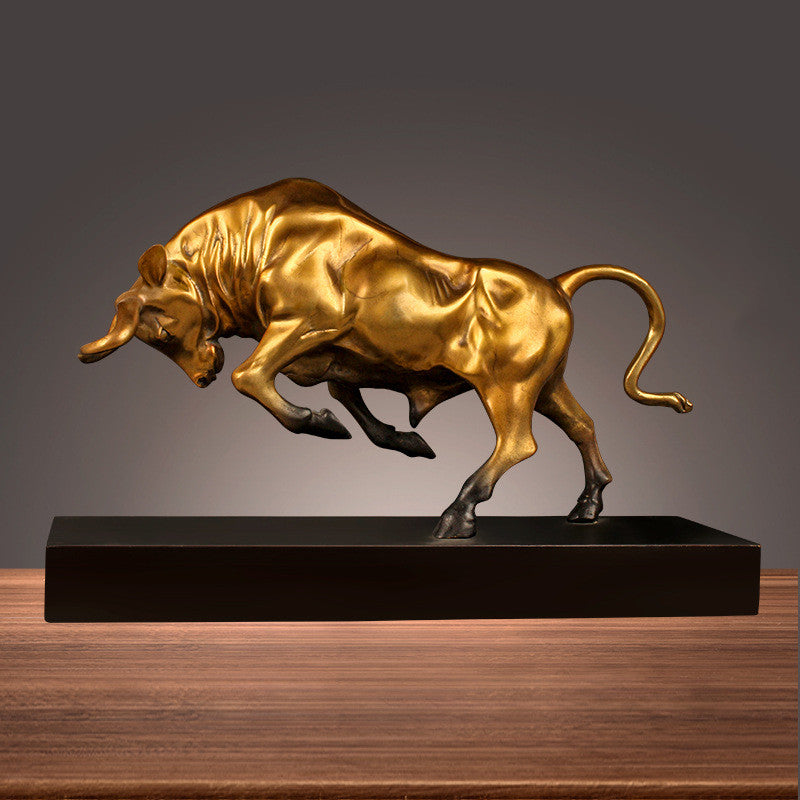 Charging bull metal sculpture in gold finish on black base, front view, freestanding on wooden surface
