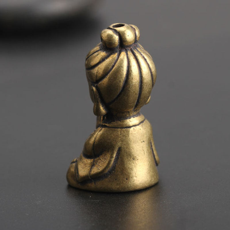 Small brass-look meditating figure ornament, back view, showing topknot and through-hole at top, on dark surface