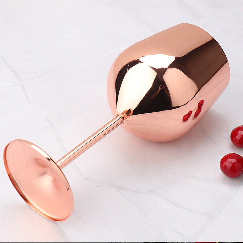 Rose gold stainless steel wine glass lying on its side on white marble background with red berries nearby
