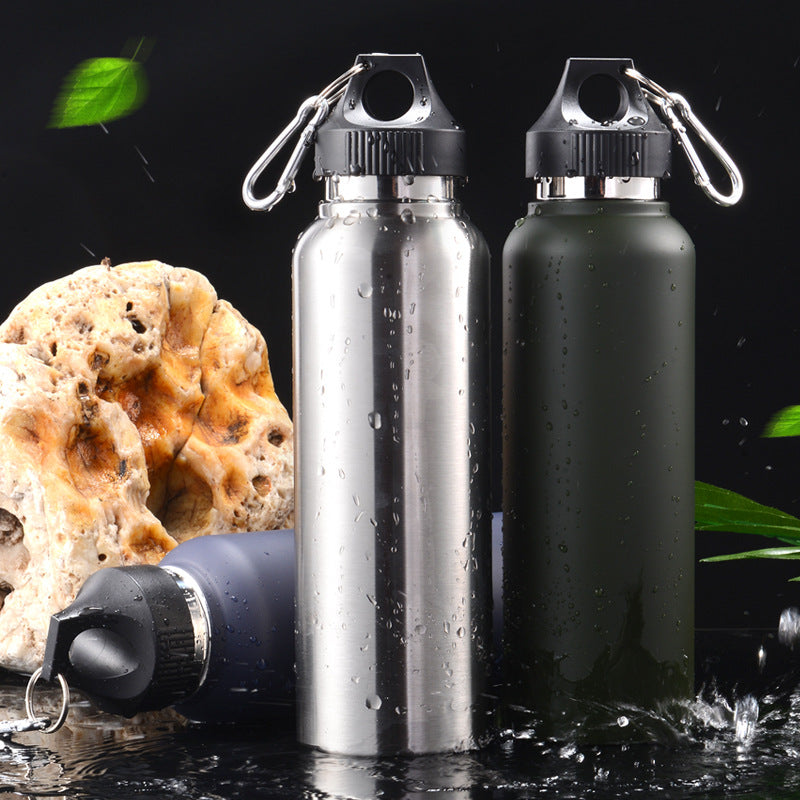Silver and olive green stainless steel vacuum bottles with carabiner lids, front view, standing in water with rocks and