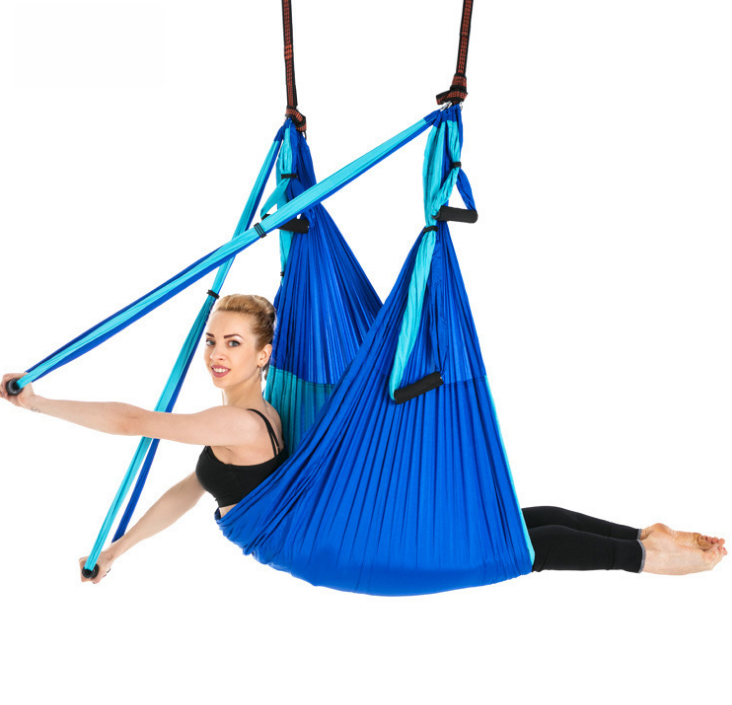 Blue aerial yoga hammock with handles, model seated in the sling holding one strap out to the side