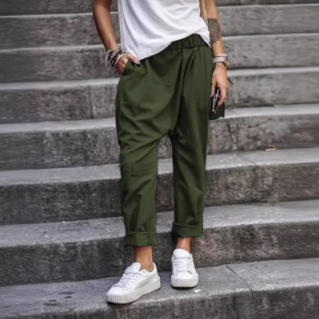 High-waist elastic harem trousers in army green, worn by a model on stone steps, front view with rolled cuffs and side