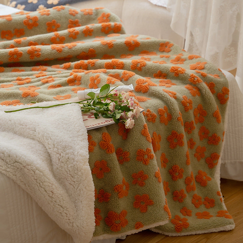 Floral jacquard sherpa-back throw blanket in sage with orange flowers, folded on a bed, showing front and reverse sides with