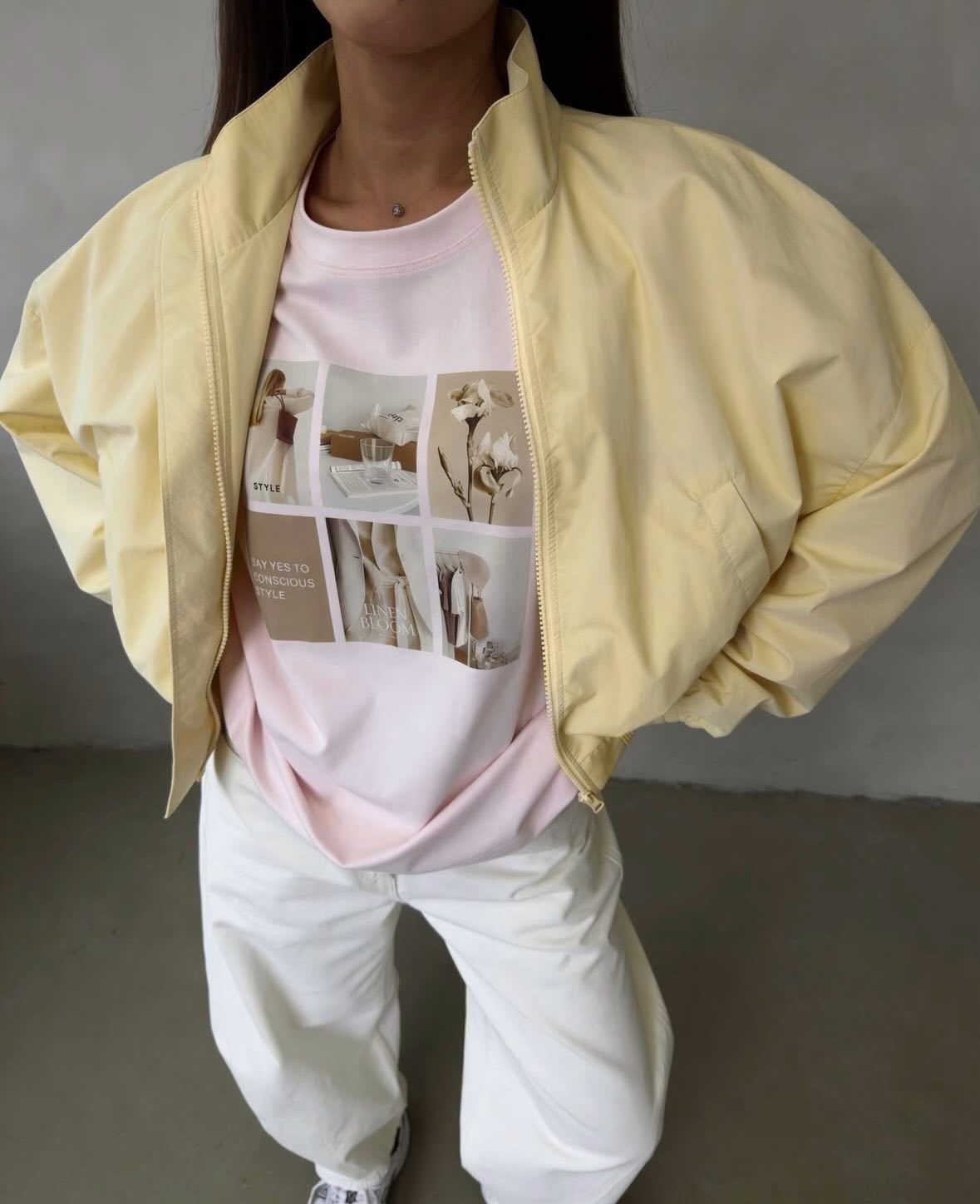 Pale yellow cropped bomber jacket, front view on model, open, hands in back, over pink graphic tee and white trousers