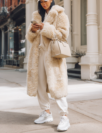 Oversized longline beige faux fur coat on model, front view, worn with light pants and sneakers, urban street setting
