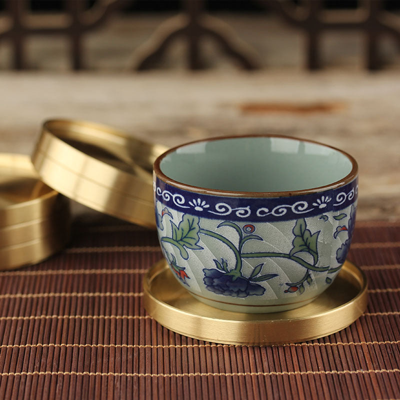Brushed gold-tone metal cup coaster with raised rim, placed under a ceramic cup on a bamboo mat