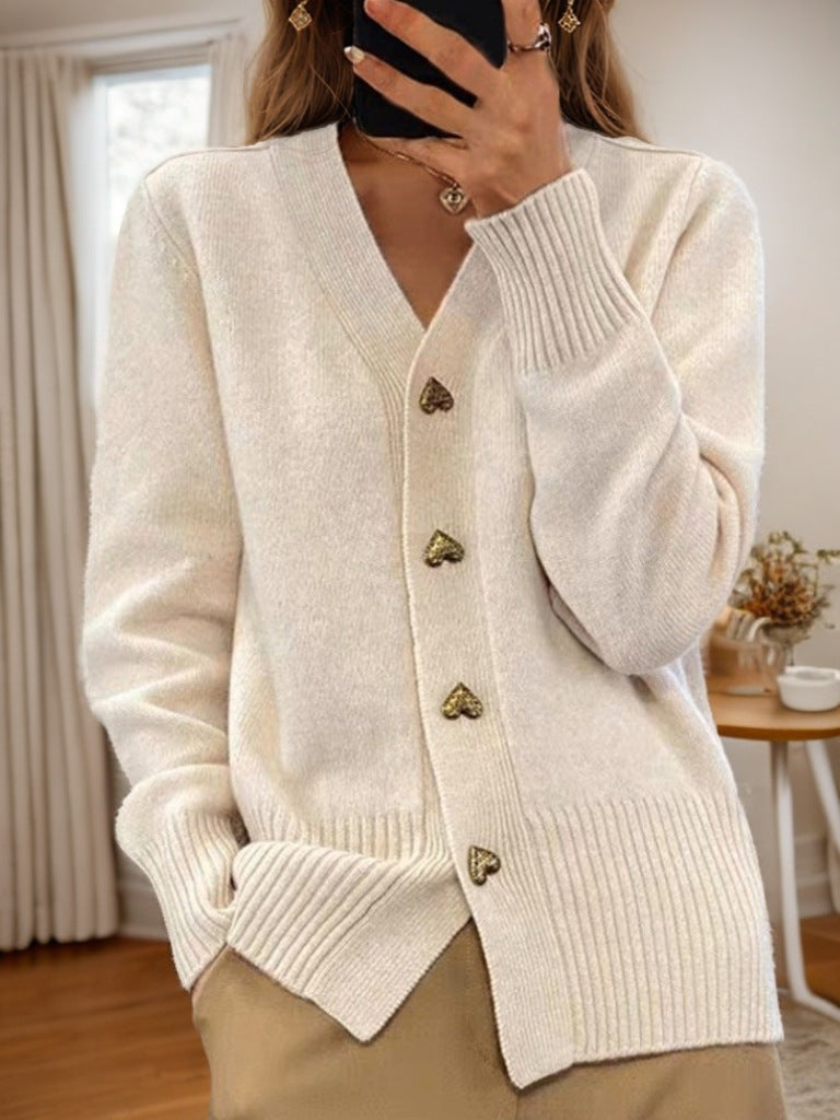 V-neck knit cardigan in off-white with heart-shaped buttons, worn by a model in a neutral-toned room