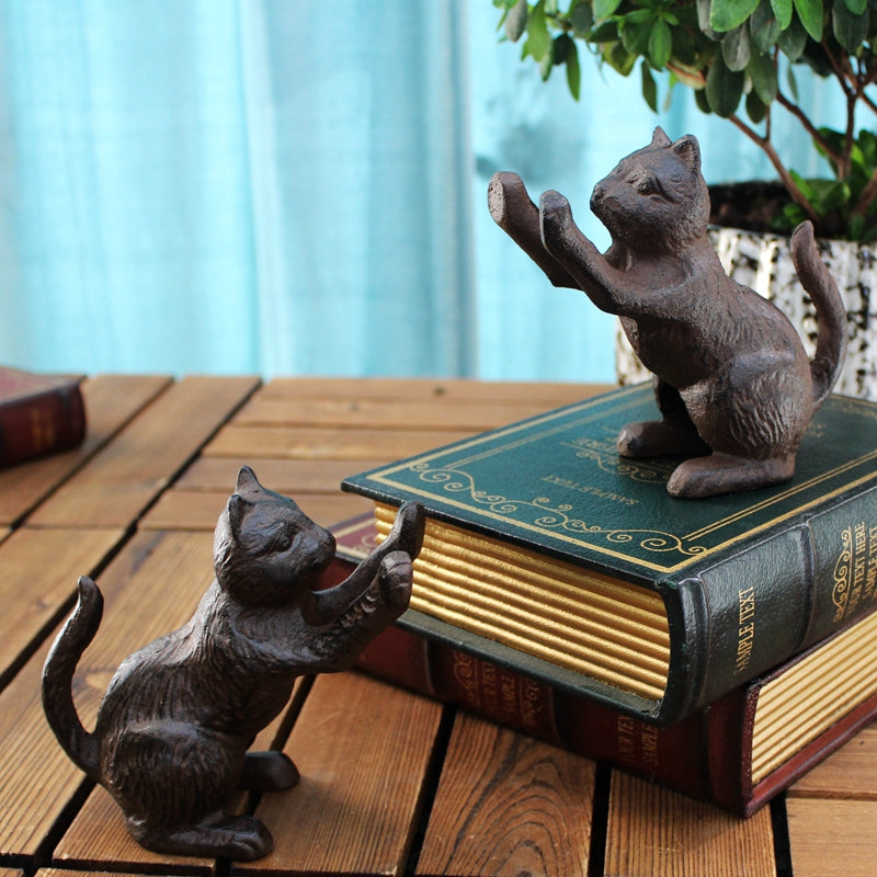 Cast-iron cat bookends, dark brown, one on top of a book, the other reaching up, side view, on wooden surface