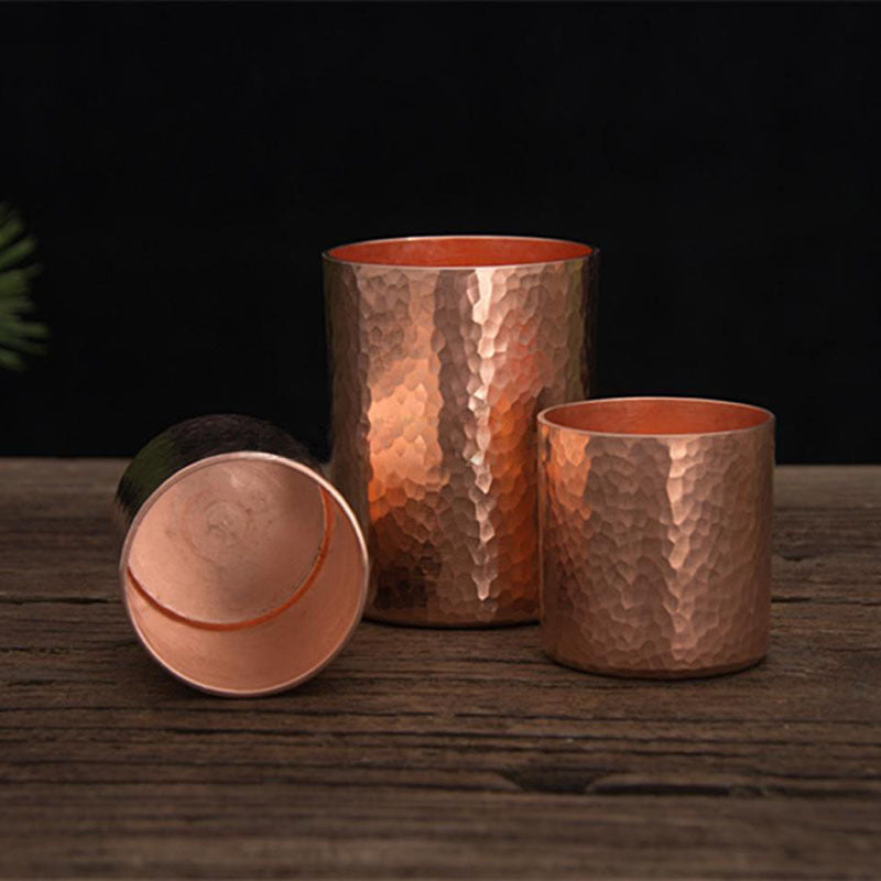 Hammered metal tea cup, copper colour, three sizes on wooden surface, one lying on side