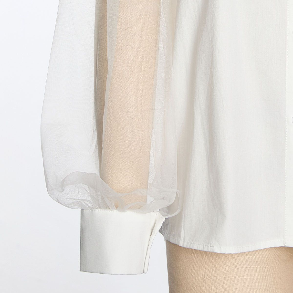 Close-up of the sheer shirt sleeve and solid white buttoned cuff on a mannequin arm