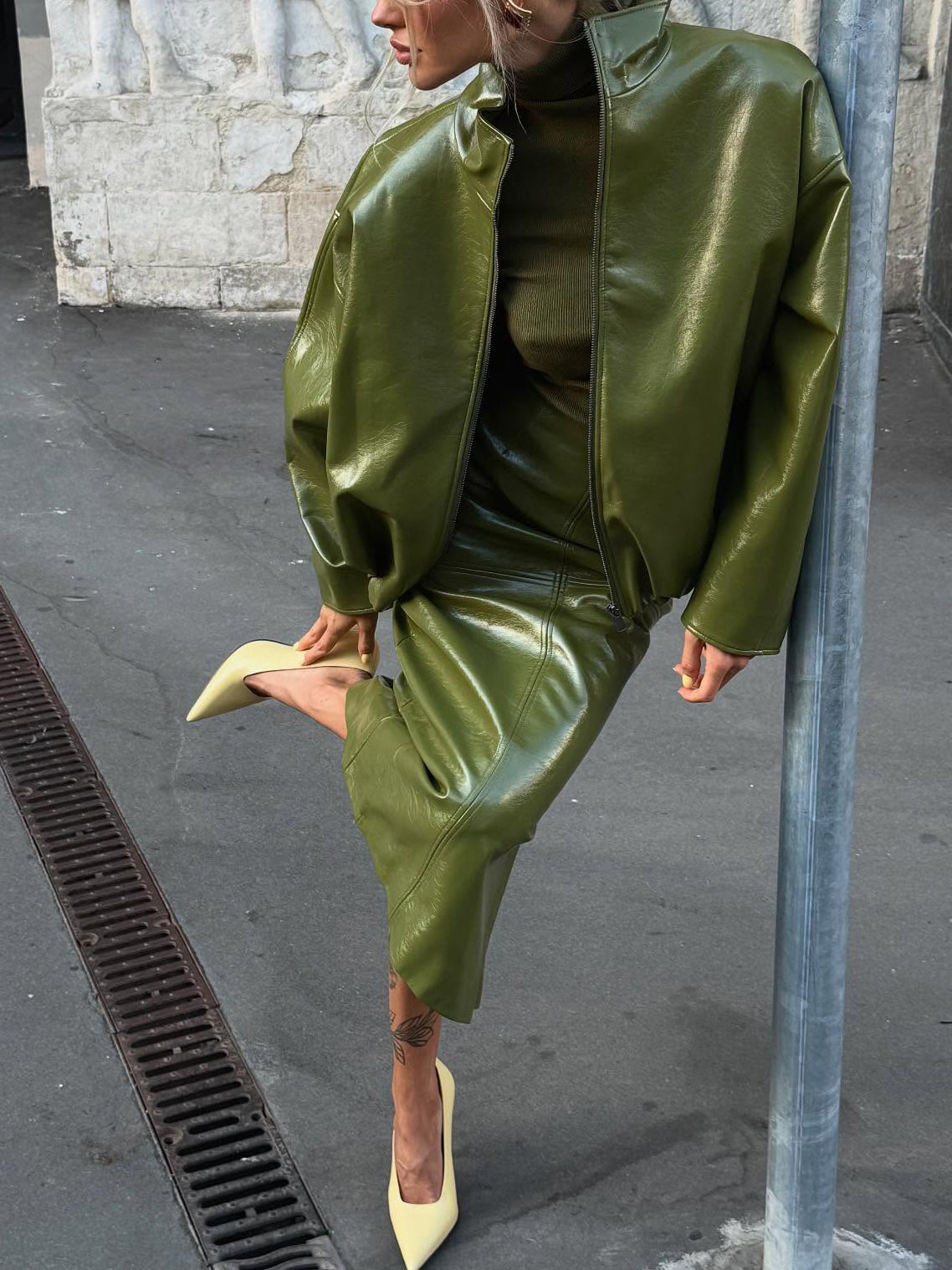 Faux-leather jacket and midi skirt co-ord set in olive green, side view on model, one foot raised, leaning against pole