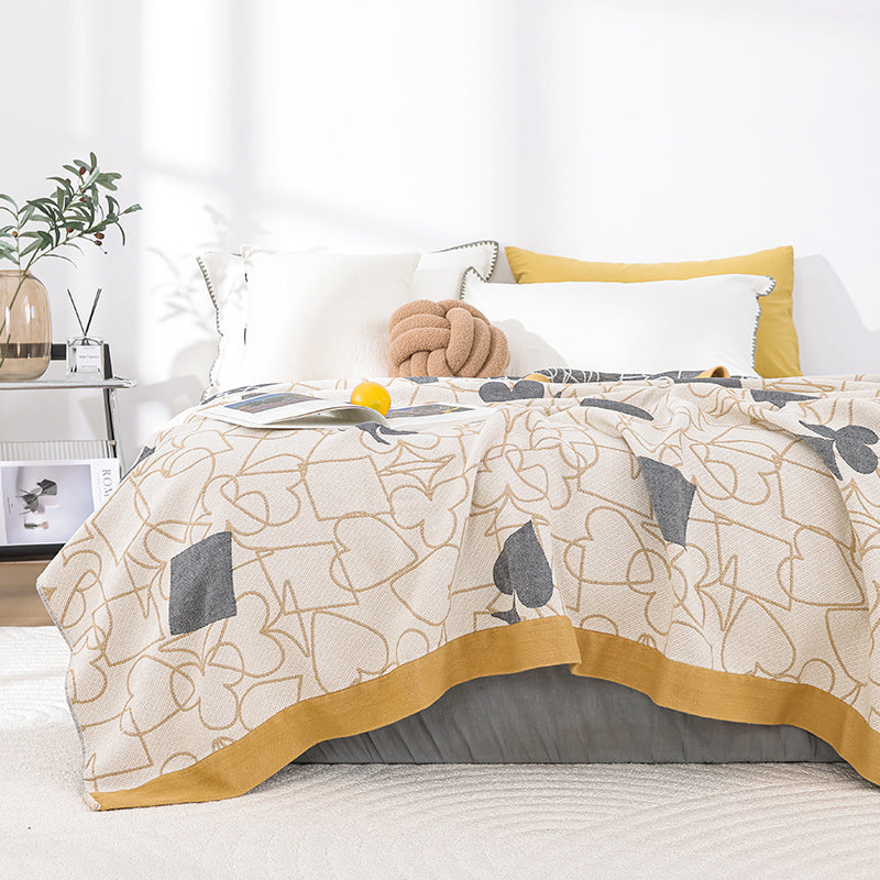Card-suit gauze blanket spread on a bed with a yellow pillow, an open book and a yellow lemon prop