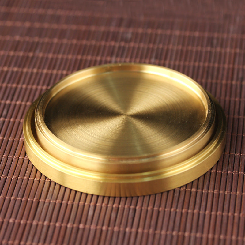 Side view of brushed gold-tone metal coaster stacked, showing raised rim on bamboo mat