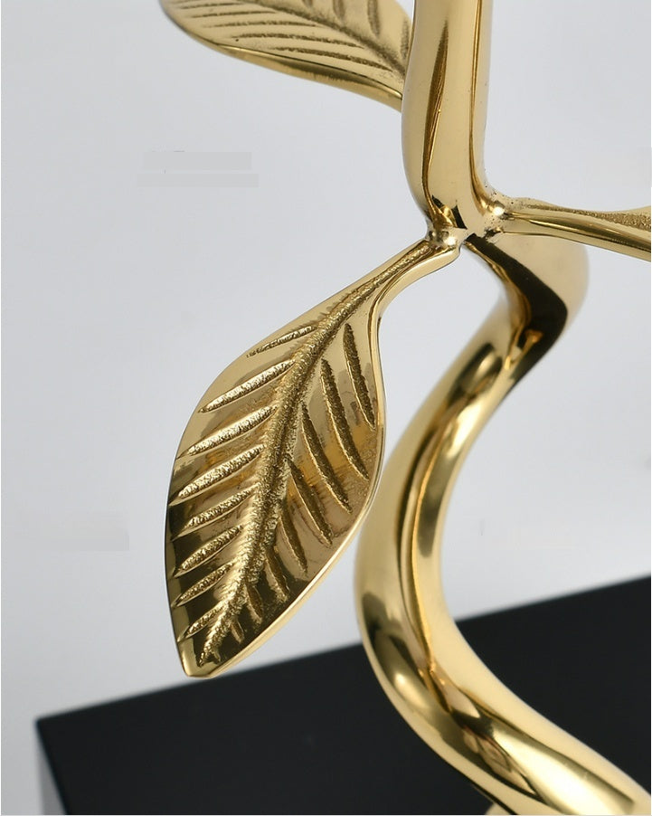 Close-up of gold-coloured stem with two detailed leaf shapes, curving design, on black square base